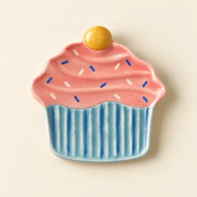 Cupcake dish painted blue and pink, with a yellow cherry and small sprinkles.