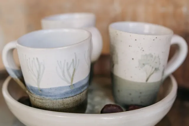 Two ceramic mugs painted with simple leaves and a band of color, in a bowl.