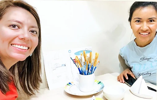 Andrea and Paola at the workshop table, with a pot of brushes and a paint palette