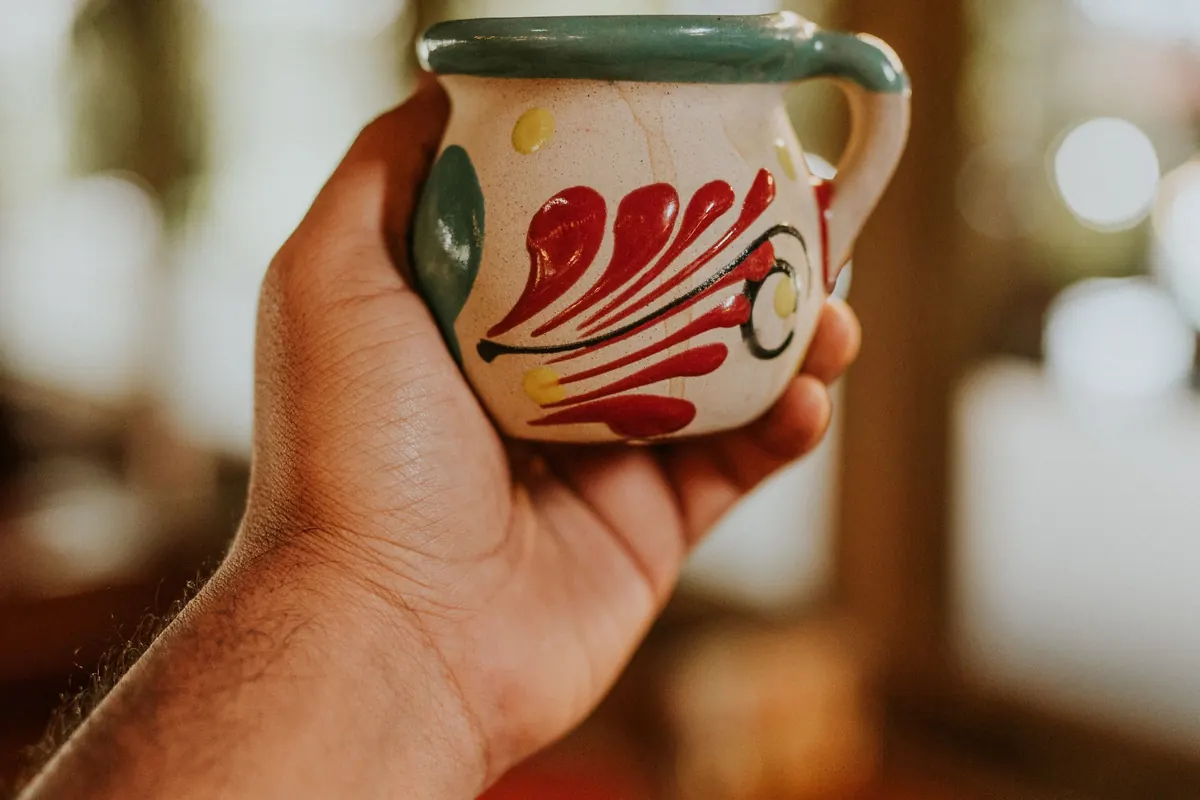 A hand holding a small painted ceramic jug.