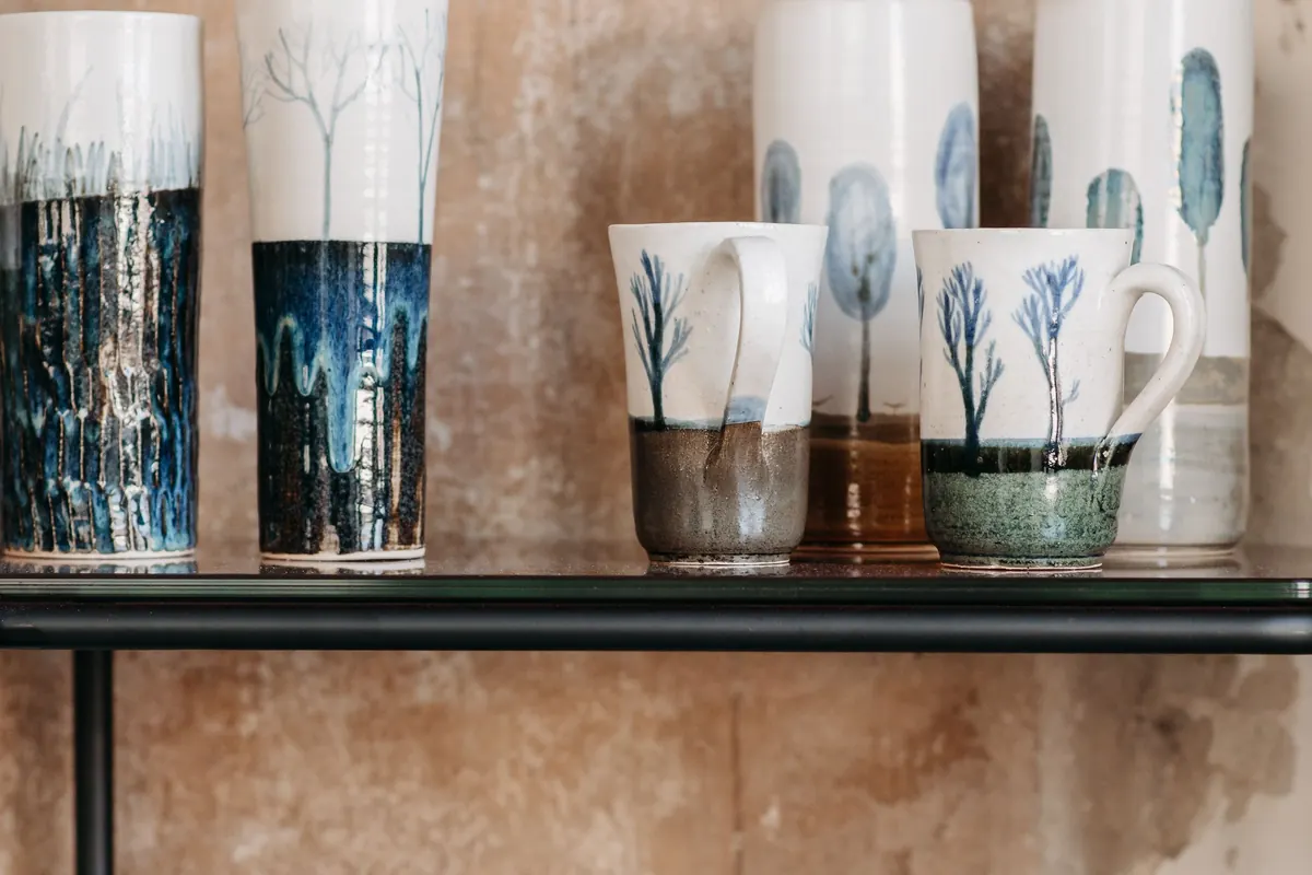 Glazed hand-painted mugs and vases on a shelf.